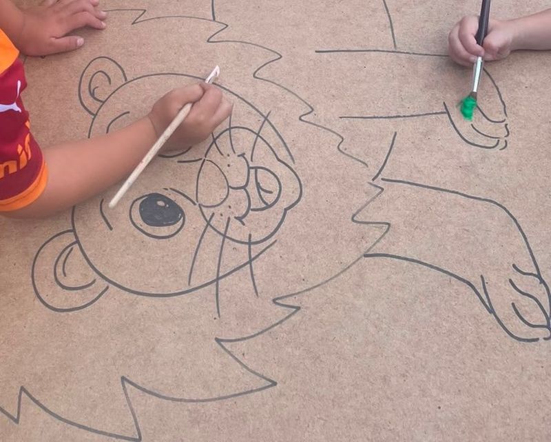 Kinderhanden schilderen samen een grote leeuw op een houten plaat